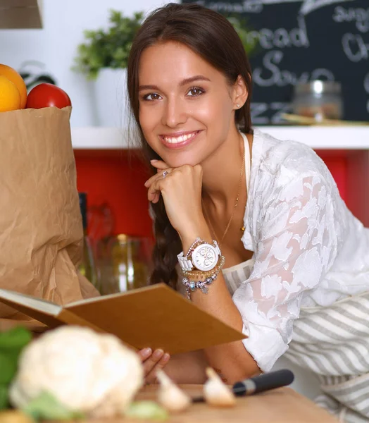 Young woman reading cookbook in the kitchen, looking for recipe — Stock Photo, Image