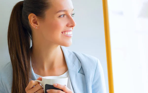 Mujer atractiva sentada en el escritorio en la oficina, trabajando con el ordenador portátil, teniendo café para llevar — Foto de Stock