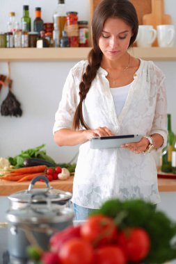 Mutfakta yemek yapmak için tablet bilgisayar kullanan genç bir kadın.