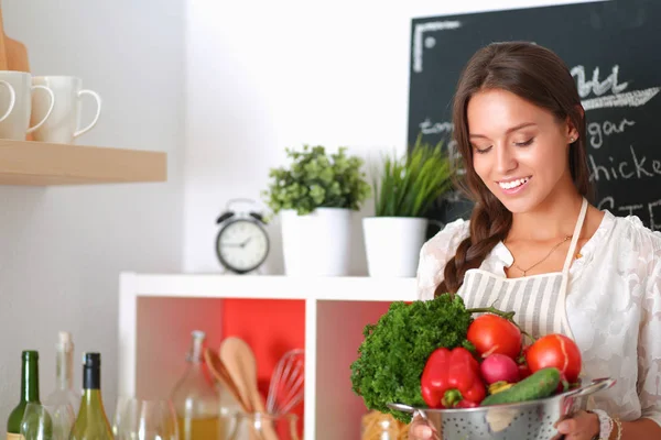 Mutfakta elinde sebzelerle gülümseyen genç bir kadın. — Stok fotoğraf