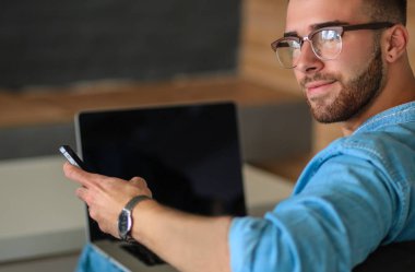 Genç adam kanepede otururken dizüstü bilgisayar ile çalışır