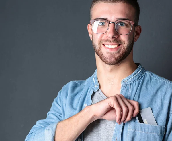 Young man holding a credit card standing on gray background — Stock Photo, Image