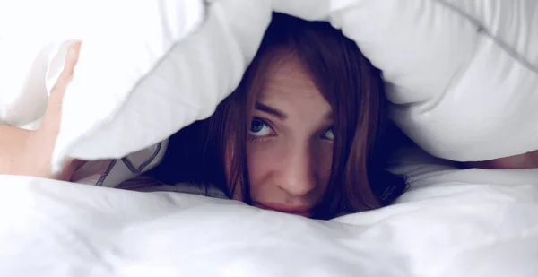 Bella giovane donna sotto il cuscino sdraiato sul letto — Foto Stock