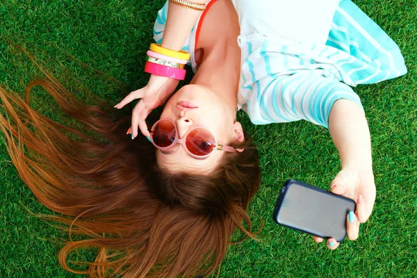 Lachende jonge vrouw liggend op het gras en het maken van een selfie — Stockfoto