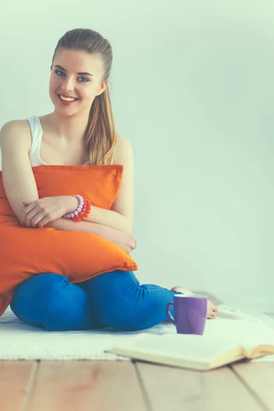 Jonge vrouw zitten met kussen en houden een kopje thee — Stockfoto