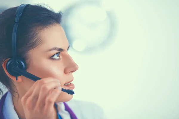 Doctor wearing headset sitting behind a desk with laptop over grey background — Stock Photo, Image