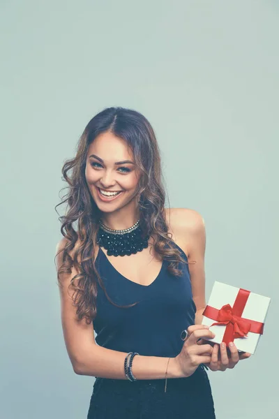 Jonge vrouw gelukkig glimlach houden de doos van de gift in handen, geïsoleerd over grijze achtergrond — Stockfoto