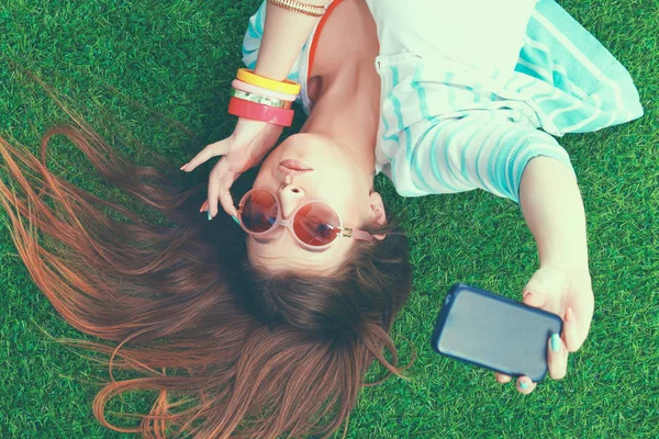 Mosolygó fiatal nő feküdt a fűben, és így a selfie — Stock Fotó