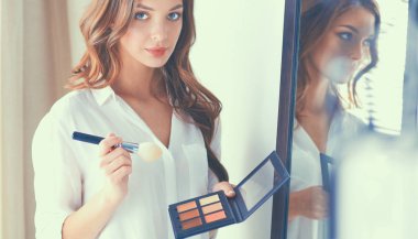 Genç ve güzel bir kadın aynanın yanında makyaj yapıyor.