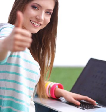 Laptoplu genç bir kadın yeşil çimlerde oturuyor.