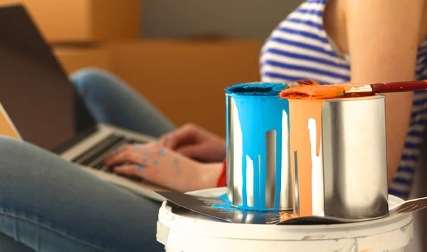 Junges Frauenporträt beim Bemalen der neuen Wohnung, sitzend mit Laptop — Stockfoto