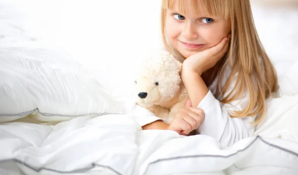 Маленькая девочка с плюшевым мишкой лежит на кровати дома — стоковое фото