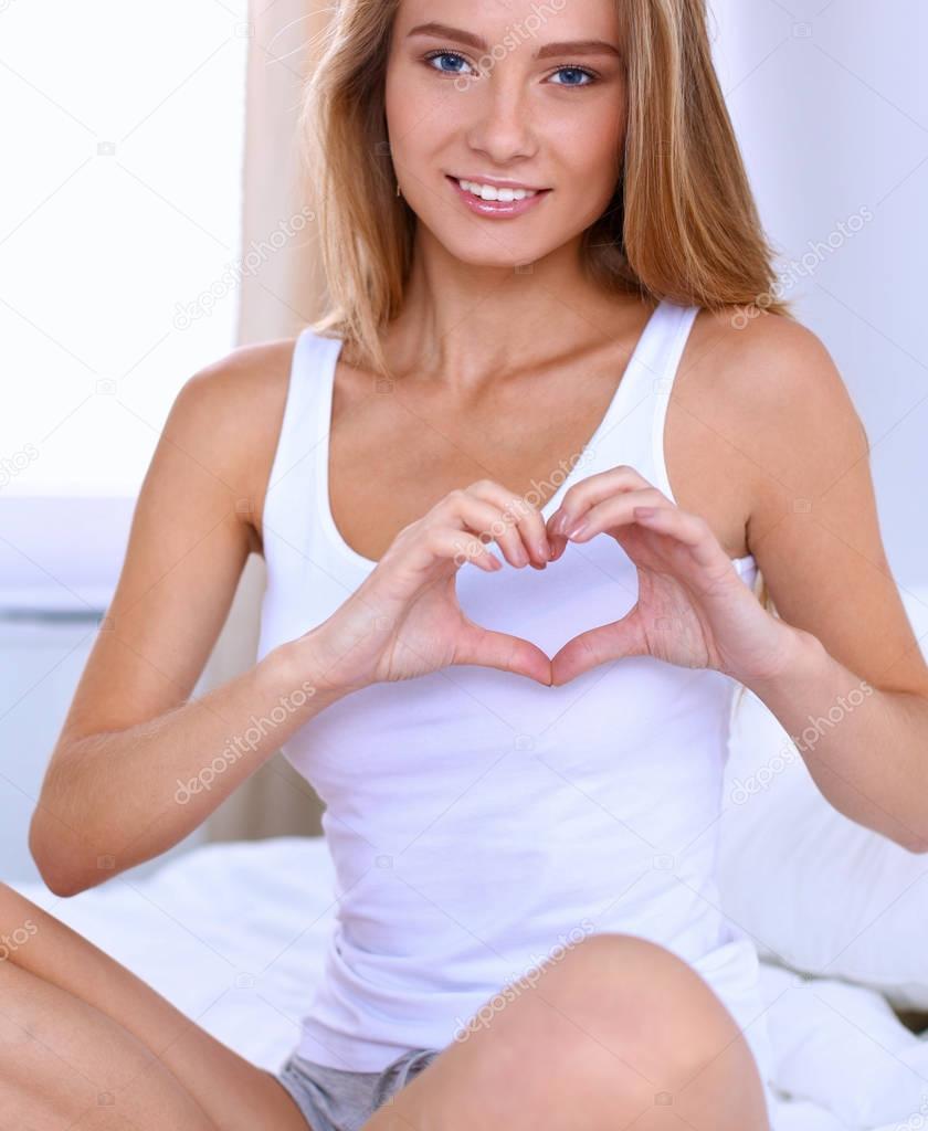 Beautiful woman showing heart shape on her hand , sitting bed