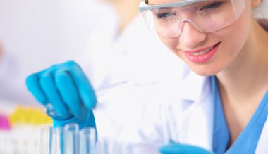 Kadın araştırmacı, beyaz arka planda izole edilmiş ilaç şişeleri ve mataralarla çevrili.