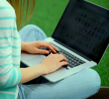 Laptoplu genç bir kadın yeşil çimlerde oturuyor.