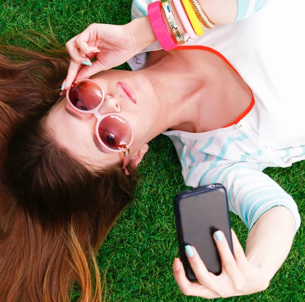 Mooie jonge vrouw selfie maken door haar telefoon liggend in groene gras — Stockfoto