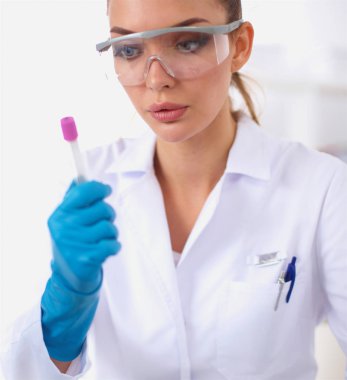 Kadın araştırmacı, beyaz arka planda izole edilmiş ilaç şişeleri ve mataralarla çevrili.