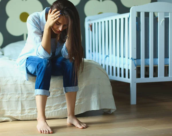 Unga trött kvinna som sitter på sängen nära barnens barnsäng — Stockfoto