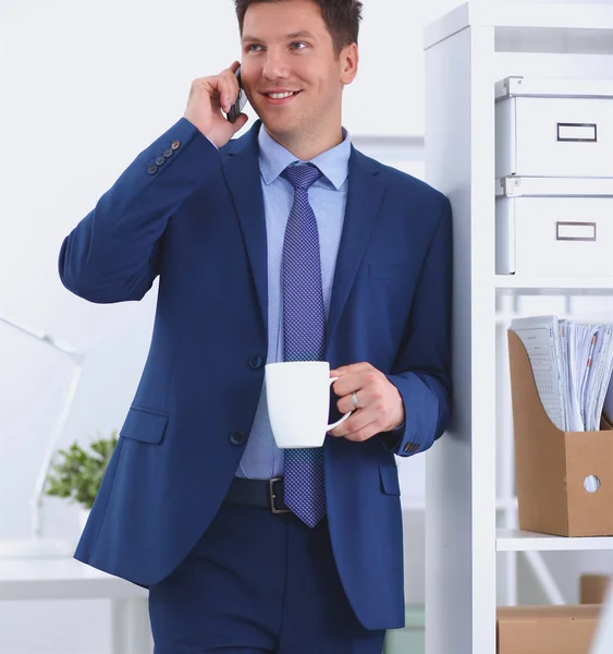 笑みを浮かべてビジネスマン立って、オフィスで携帯電話を使用して — ストック写真