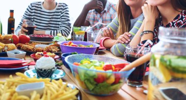 Bir grup insan ahşap masada otururken birlikte yemek yiyorlar.