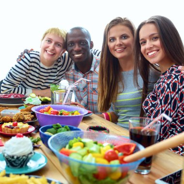 Bir grup insan ahşap masada otururken birlikte yemek yiyorlar.
