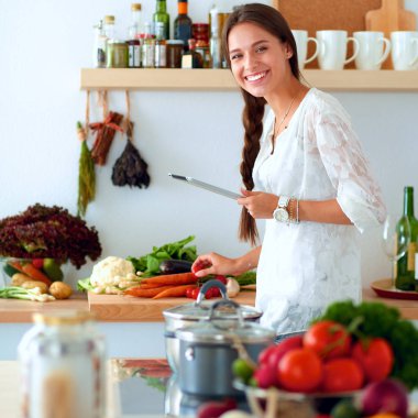 Mutfakta yemek yapmak için tablet bilgisayar kullanan genç bir kadın.