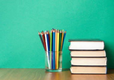 Kitaplar ve renkli kalemler yeşil zemin üzerine yığını