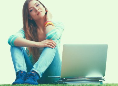 Laptoplu genç bir kadın yeşil çimlerde oturuyor.