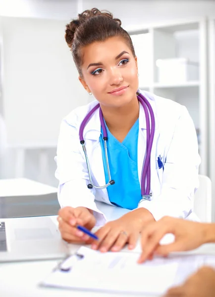 Hermosa joven sonriente doctora sentada en el escritorio y escribiendo. —  Fotos de Stock