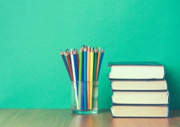 Пачка книг и цветных карандашей на зеленом фоне — стоковое фото