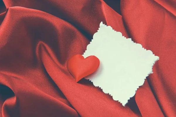 หัวใจสีแดงและโปสการ์ดสีขาวว่างเปล่า นอนอยู่บนผ้าไหม — ภาพถ่ายสต็อก