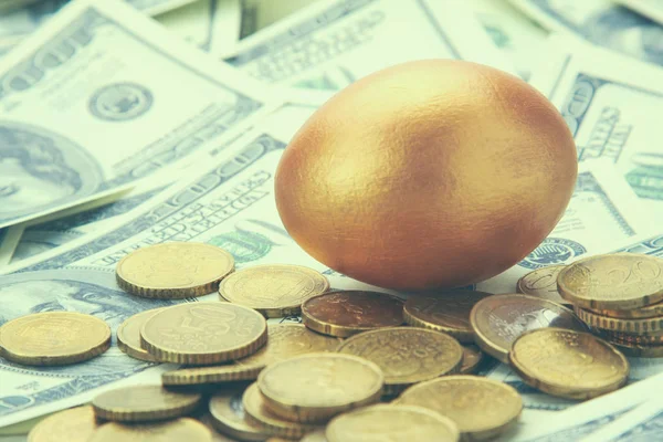 Een gouden ei liggen op dollar en munten — Stockfoto