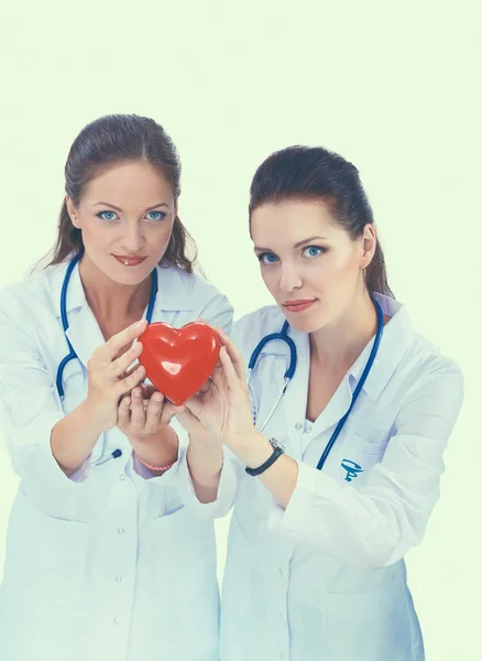Kırmızı kalp taşıyan iki kadın doktor, beyaz arka planda izole edilmiş. — Stok fotoğraf