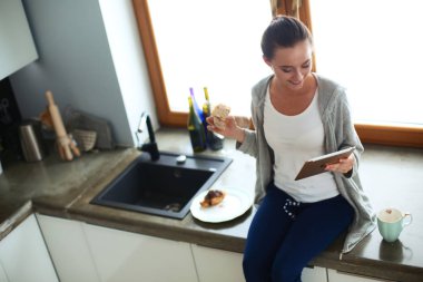 Mutfakta dijital tablet kullanan güzel genç bir kadın.