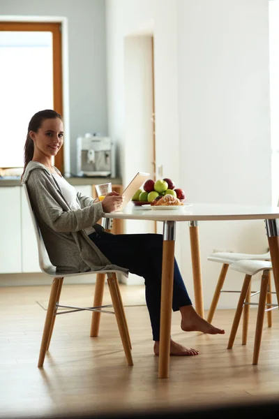 Ung kvinna med apelsinjuice och tablett i köket — Stockfoto