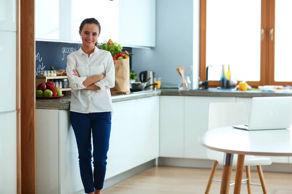 Retrato de mujer joven de pie con los brazos cruzados contra el fondo de la cocina — Foto de Stock