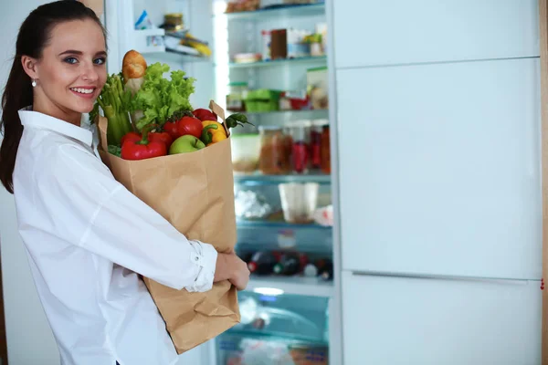 Jovem mulher segurando supermercado saco de compras com legumes .Standing na cozinha — Fotografia de Stock