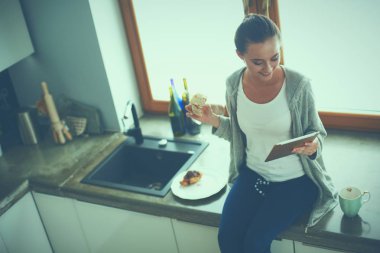 Mutfakta dijital tablet kullanan güzel genç bir kadın.