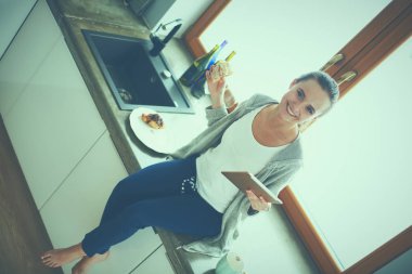 Mutfakta dijital tablet kullanan güzel genç bir kadın.