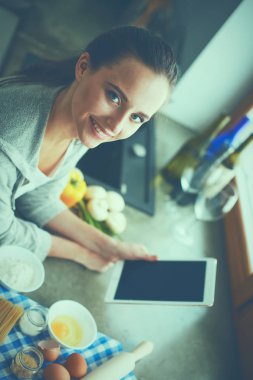 Tablette tarifi takip eden bir kadın evde yemek pişiriyor.