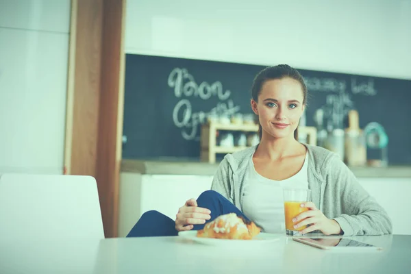 Mujer joven con jugo de naranja y tableta en la cocina —  Fotos de Stock