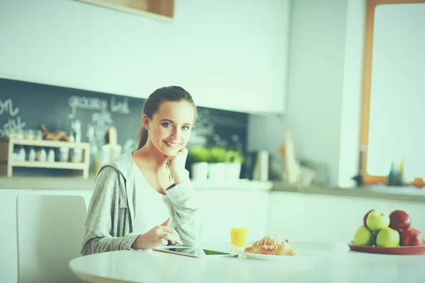 Ung kvinna med apelsinjuice och tablett i köket — Stockfoto
