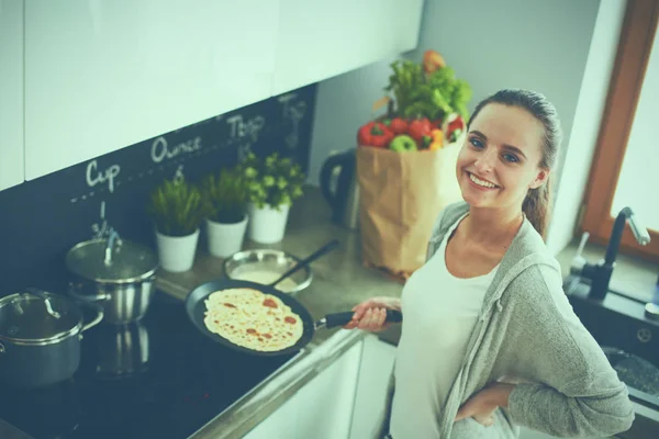 Mujer joven cocinando panqueques en la cocina de pie cerca de la estufa —  Fotos de Stock