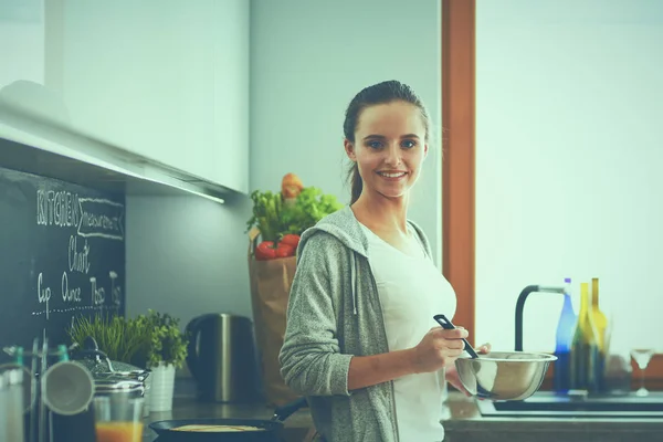 Ung kvinna matlagning pannkakor i köket står nära spis — Stockfoto