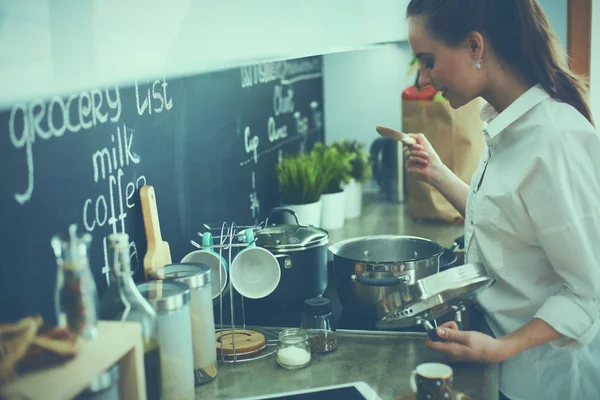 Mujer joven parada junto a la estufa en la cocina — Foto de Stock