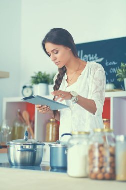 Mutfakta yemek yapmak için tablet bilgisayar kullanan genç bir kadın.