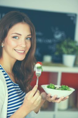 Genç bir kadın salata yiyor ve karışık bir şey tutuyor.