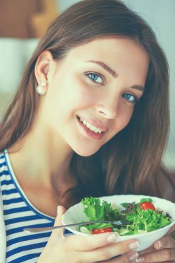 Genç bir kadın salata yiyor ve karışık bir şey tutuyor.