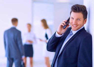 Ofisteki genç iş adamının portresi. Arka planda meslektaşları var ve cep telefonu kullanıyor.