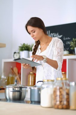 Mutfakta yemek yapmak için tablet bilgisayar kullanan genç bir kadın.